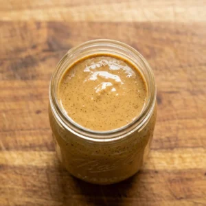 Overhead view of smooth and creamy almond butter inside a glass mason jar on a wooden cutting board.