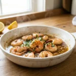 A rustic white skillet filled with juicy shrimp roasted in garlic butter garnished with fresh parsley and lemon wedges.