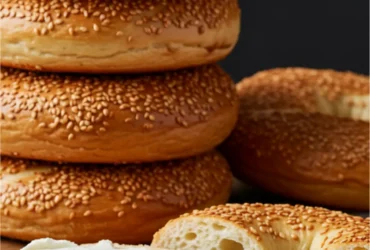 A beautiful stack of freshly baked Montreal bagels, with one sliced open and generously spread with cream cheese on a rustic wooden board.