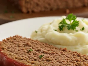 A thick, juicy slice of the finished Lipton Onion Soup Mix Meatloaf recipe on a white plate, showcasing its moist texture and caramelized ketchup glaze, served next to mashed potatoes.