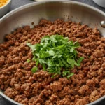 A stainless steel skillet filled with juicy, perfectly seasoned ground beef taco meat, garnished with fresh cilantro, ready to be served for an easy weeknight dinner.